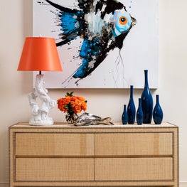 A large painting of a single tropical fish tops a raffia credenza.