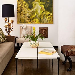 A loft's lounge is layered in tones of green and mustard against a crisp white backdrop and accented by many textures including gilt, marble, ceramic, velvet, concrete, and rich mahogany.