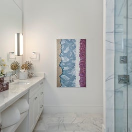 White marble bathroom, with glass shower, mirror wall sconces and abstract art.