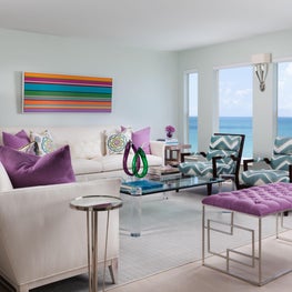This neutral spacious living room has pops of purple and luscious ocean views.