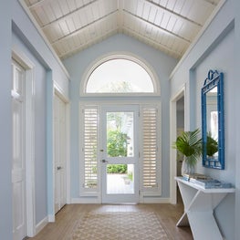 Tropical hallway with high paneled ceiling and arched window.