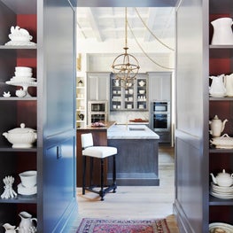 Custom shelving leading into kitchen with statement lighting and coffered ceiling