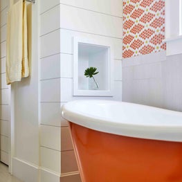 Pops of orange create a cheerful guest bathroom complete with deep soaking tub