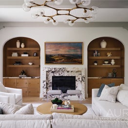 A bold marble fireplace anchors the living room, complemented by custom built-ins and reeded shelving that balance sculptural presence with softness.