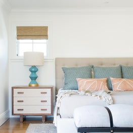 Luxurious, eclectic master bedroom with geometric lamps and teal and coral hues.