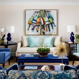 A pair of blue table lamps flank an ivory sofa with cerulean throw pillows. 