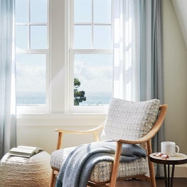 Blue and white coastal bedroom with upholstered chair and sheer curtains