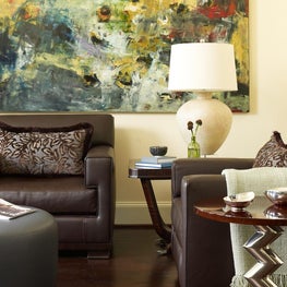 An intimate corner for conversation features a pair of leather club chairs, a complementary leather ottoman, sleek side tables, and extraordinarily colorful modern art.