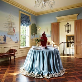 This decorative hallway has inlaid hardwood floors and blue draped round table.
