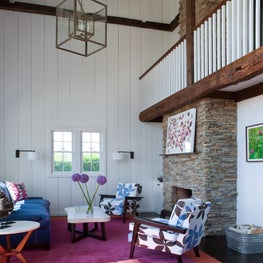 Hamptons barn house living room with wood beams, pops of color, and fireplace