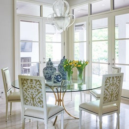 Louis XVI-style chairs surround a glass-top table with a custom gold-leaf base. Blue and white delft porcelain complements the golden tones.