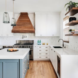 White kitchen with gray-green custom island, wood hood, Wolf range, wine fridge.