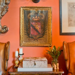 Antiques are showcased on and in front of a rich, red-orange painted wall.