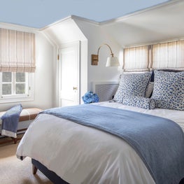 Bedroom w herringbone rug, camel bench, blue ceiling, white walls, brass sconces