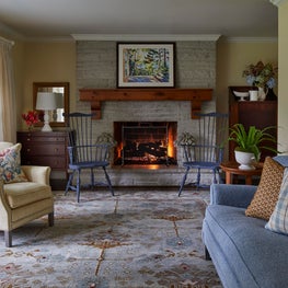 Glenview Foyer. Stone fireplace with natural wood beam mantle, navy windsor chairs & blue, chamois and red accents.