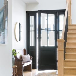 Welcoming farmhouse entry with black door and sidelights, wood staircase.