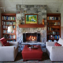 Three Barn Farm Library. Rustic farmhouse stone fireplace with built-in wood shelving & lounge seating.
