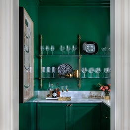 Striking bar with lacquered walls, wallpapered ceiling, & custom brass shelving