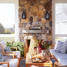 Coastal porch with blue and white outdoor furniture and stone fireplace