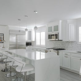 Modern all white kitchen with waterfall quartz slab on centralized island 