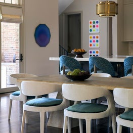 Portfolio: A cerused dining table is surrounded by upholstered chairs with teal accents, while colorful artwork and brass lighting energize this breakfast room.