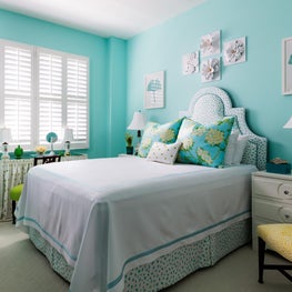 A relaxing bedroom with soft blue walls, and cheerful prints.