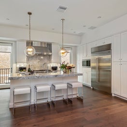 Open kitchen with large island, leather stools and sphere pendant lighting.