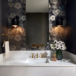 A moody powder room wrapped in shimmery wallpaper, brought to life by sculptural sconces and a touch of dramatic charm.