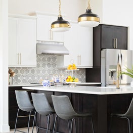 Leather counter stools pulled up to white marble breakfast bar w/pendant lights