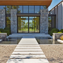 Water rills pour into a reflecting pool traversed by stone pavers at entrance