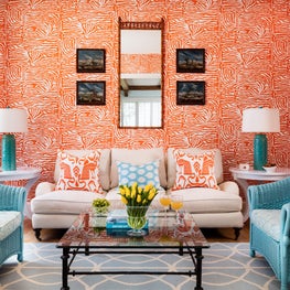 Abstract orange wallpaper is complemented by light blue wicker chairs.