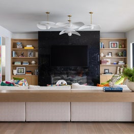 Portfolio: A living room vignette boasts a dramatic black stone fireplace framed by white oak shelving, sculptural lighting, and colorful contemporary furnishing