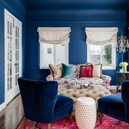 Colorful home office sitting area with blue chairs, blue walls, and pink rug