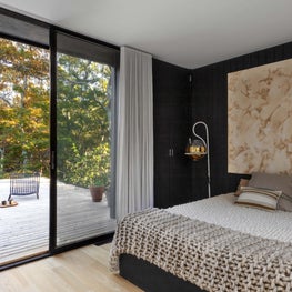 Modern bedroom with warm accents, glass wall overlooking outdoor patio