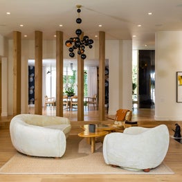 Family Room with Curved Jean Royere Sofa and Armchair that Contrast Against Vertical Oak Columns - Trousdakle Estates 