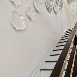 Rich wood staircase with white walls decorated with ceramic carnation wall art.