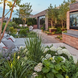 Outdoor TV, daybed and dining areas on lushly-planted rooftop terrace