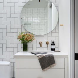 Bright, white bath with geometric tiled wall, round mirror, and leather-handled vanity