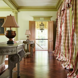 Finely carved furniture in a room with coffered ceilings and voluminous drapery.