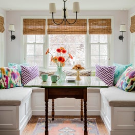 Bright and cheerful breakfast nook banquette colorful pillows antique table
