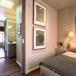 Calming master bedroom with wood flooring and stacked artwork