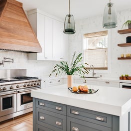 White kitchen with gray-green custom island, wood hood, Wolf range, wine fridge.