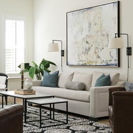 Neutral living room with bold artwork, paneled ceiling and occasional tables.