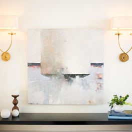 Waterfall console table w/ brass sconces & modern art, design by Sophia Shibles