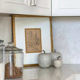 Portfolio: Corner view of a modern kitchen with white marbling and cabinetry for a softened glamour.