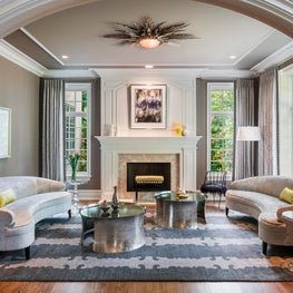 Curved sofas, a fabulous ceiling light and the bracelet style cocktail tables play nicely with the traditional architecture in this chic living room