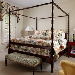 A dark wood four post bed and furniture juxtaposes the neutral walls and carpets