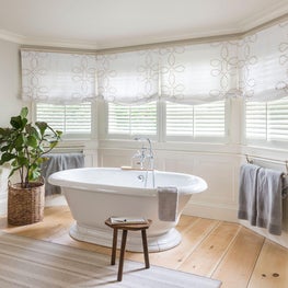 Bathtub in bay window w graphic linen roman shades striped wool rug
