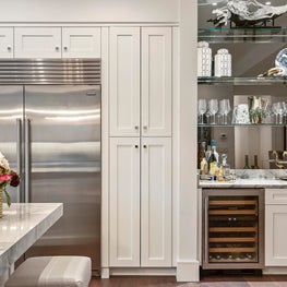 Floor-to-ceiling white cabinets, bar with wine fridge and mirrored open shelves.