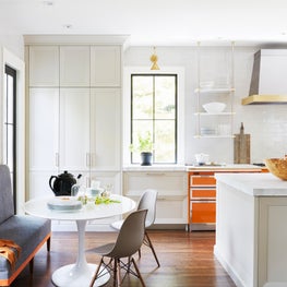 Bright white kitchen with pops of orange, brass accents, and banquette seating